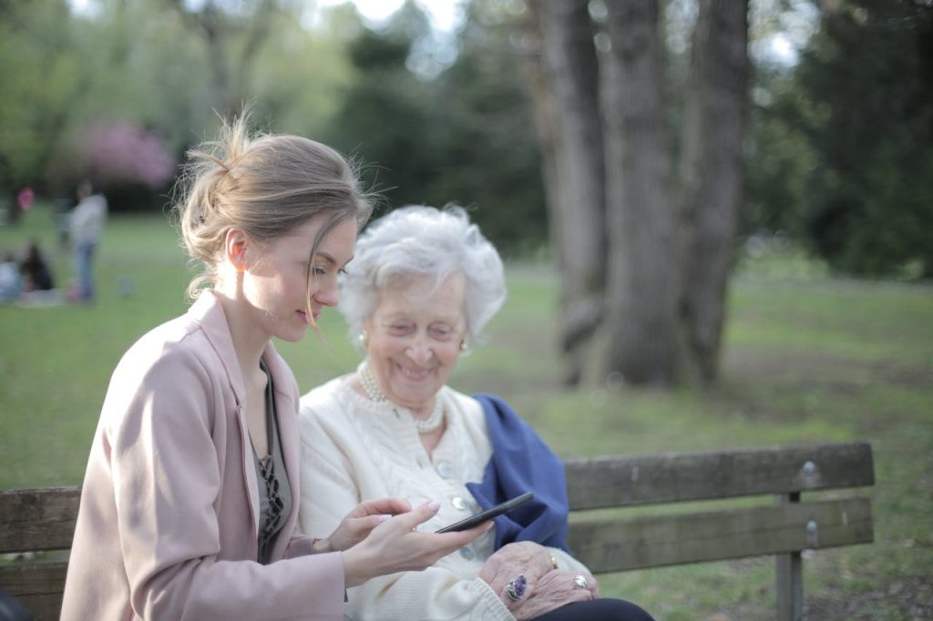 pexels photo 3791666 Side view of smiling adult female helping aged mom in using of mobile phone while sitting together in park